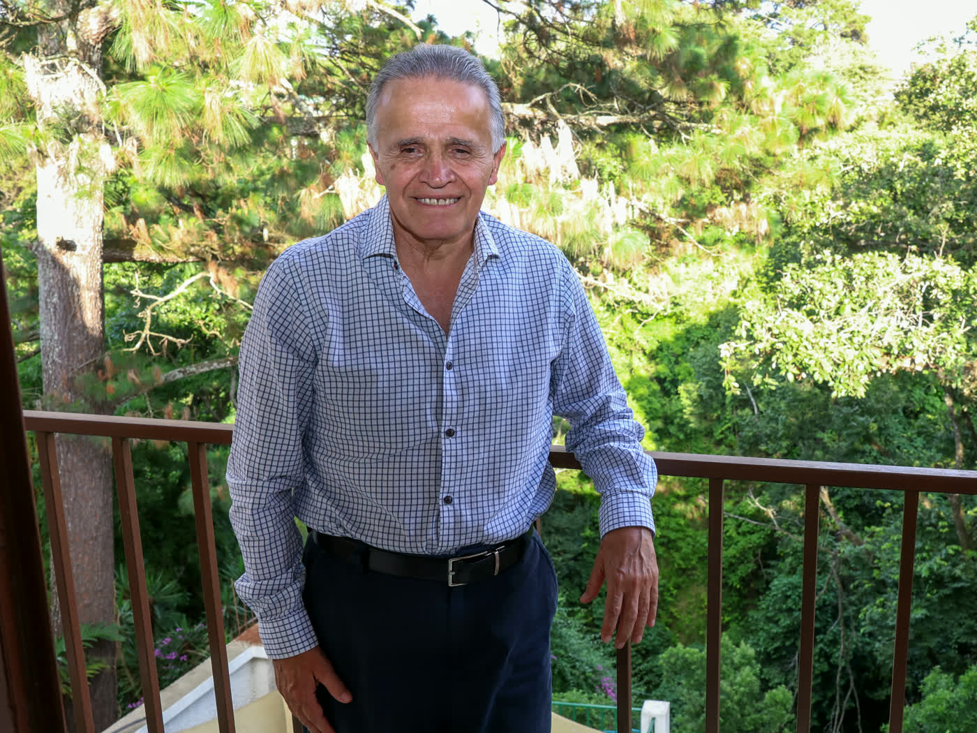 Lic. Fernando Estrada de pie, sonriendo, rodeado de vegetación